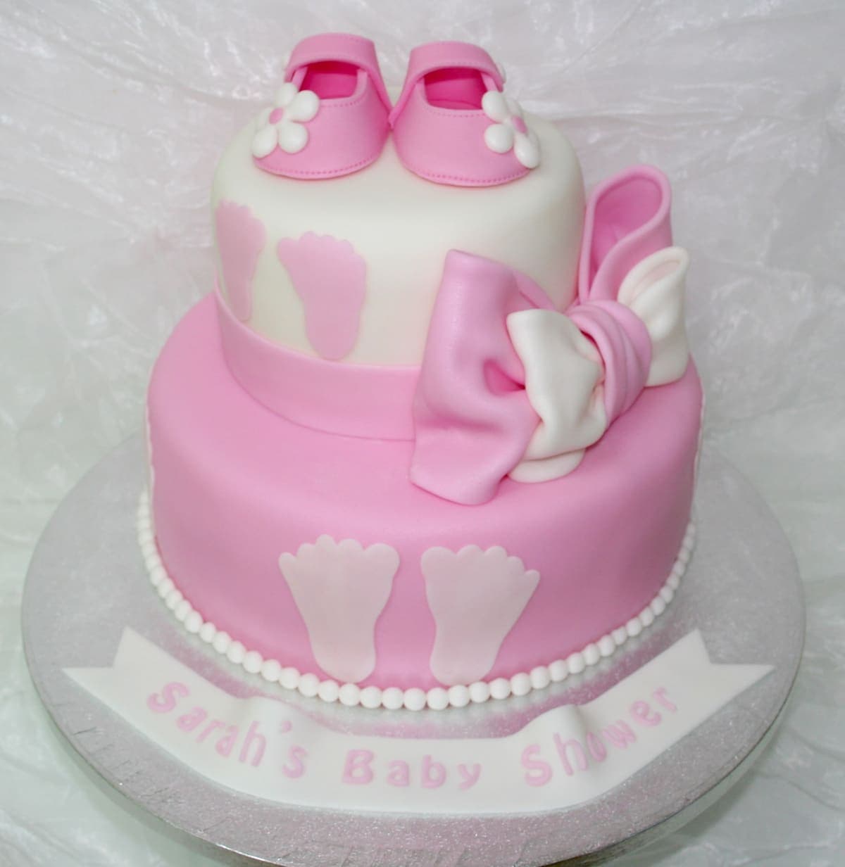 Rosa Babytorte mit Babyschuhen, Fußabdrücken und Schleife