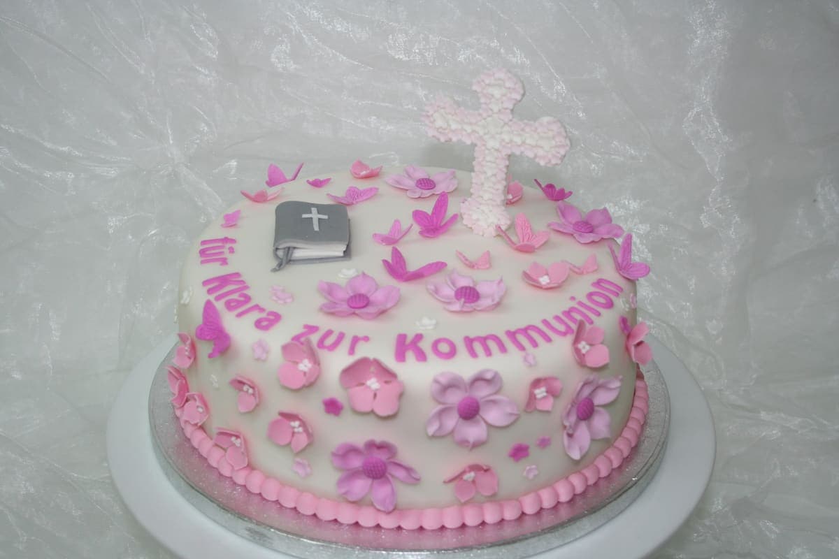 Elegante Kommuniontorte mit rosa Blüten und Kreuz