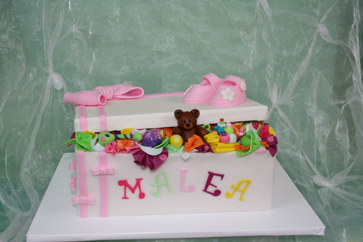 Kreative Spielzeugkiste-Torte mit buntem Spielzeug und rosa Babyschuhen